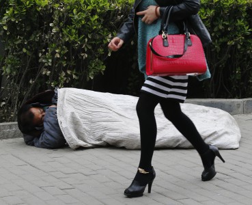 A woman walks past a homeless man sleeping on the street in Beijing